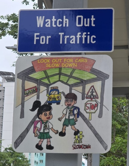 Student-designed traffic safety artwork displayed beneath a road safety sign.